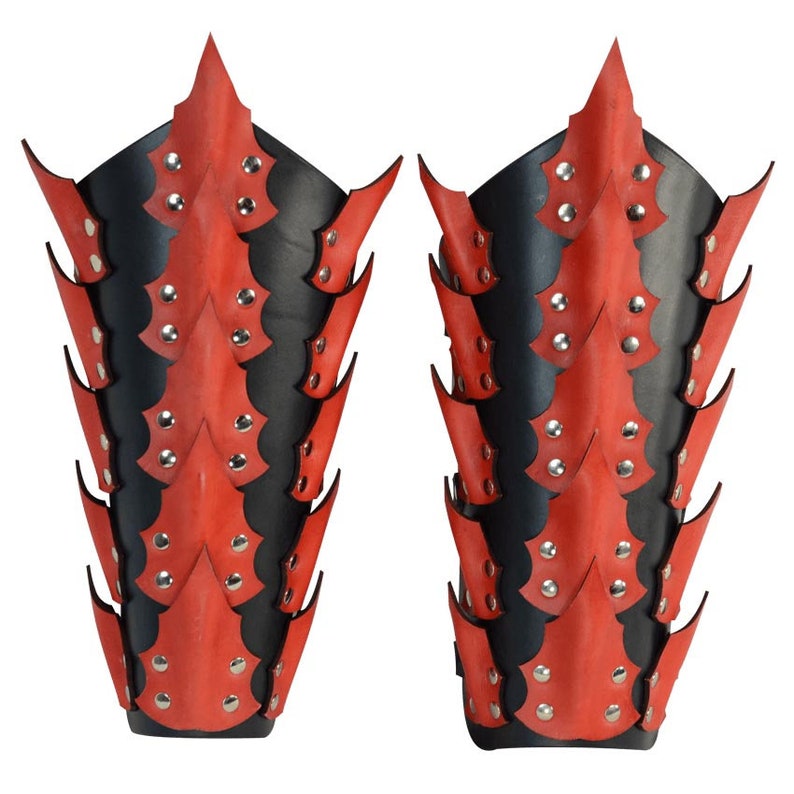 Op de afbeelding: Een paar rode en zwarte leren armbeschermers met een stekelig ontwerp. De beschermers zijn versierd met zilveren studs.