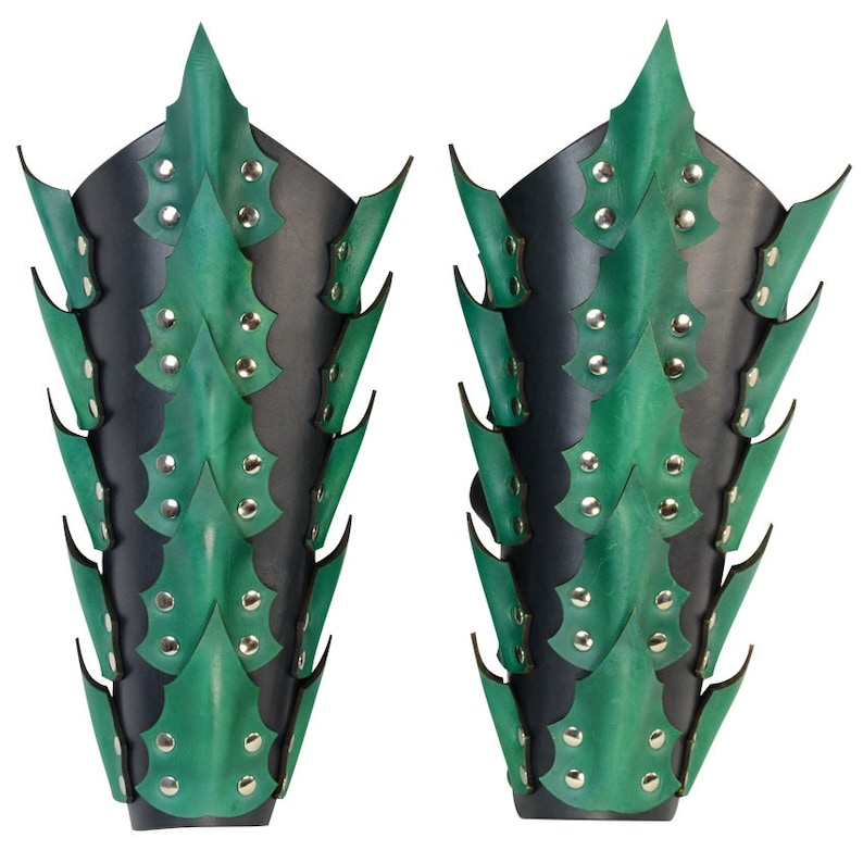 Op de afbeelding: Een paar groene en zwarte leren armbeschermers met een stekelig ontwerp. De beschermers zijn gemaakt van leer en hebben een reeks stekels die langs de lengte van de arm lopen. De stekels zijn gemaakt van metaal en zijn met klinknagels aan het leer bevestigd.