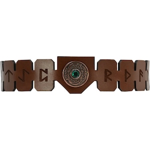 May include: Brown leather bracelet with a metal charm featuring a green gemstone and a Celtic knot design. The bracelet is decorated with runes.