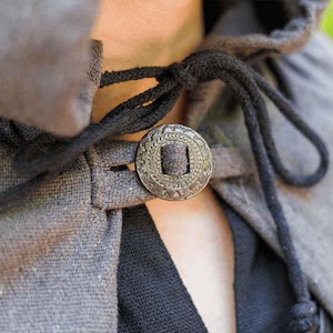 May include: A gray hooded cloak with a black drawstring and a decorative metal button. The button has a circular design with a raised center.
