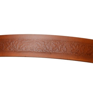 Op de afbeelding: Een close-up van een bruine leren riem met een reli&euml;fpatroon van bladeren.