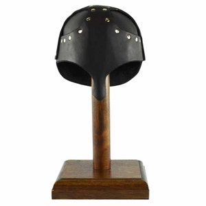 Puede incluir: Casco de cuero negro con remaches de lat&oacute;n, exhibido en un soporte de madera.