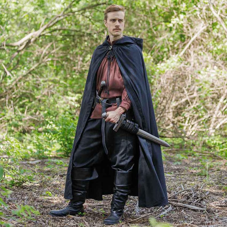May include: A person wearing a black hooded cloak with a brown shirt and black pants. They are holding a sword in their right hand.