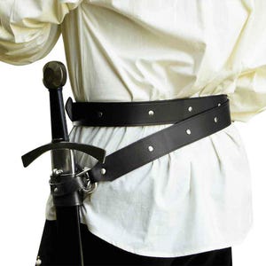 May include: A black leather sword belt with silver-toned metal rivets and a matching black leather scabbard holding a sword with a dark handle and a silver crossguard, worn over a cream-colored long-sleeved shirt with a loose, gathered fit.