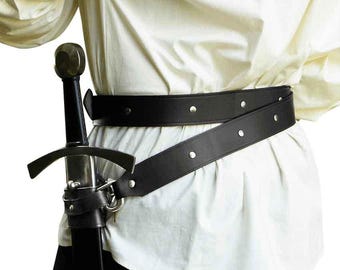 Puede incluir: Un cinturón de espada de cuero negro con remaches metálicos plateados y una funda de cuero negro a juego que sostiene una espada con mango oscuro y guarda plateada, usado sobre una camisa de color crema de manga larga con ajuste holgado.