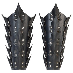 Op de afbeelding: Een paar zwarte leren armbeschermers met een stekelig ontwerp en zilveren studs.