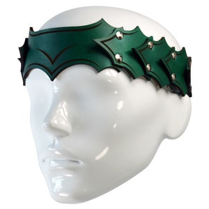 May include: A green leather headband with a pointed design and silver studs. The headband is worn on a white mannequin head.