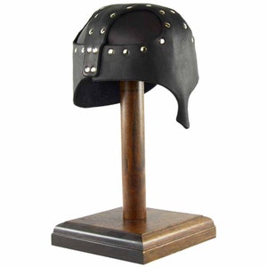 Puede incluir: Un casco de cuero negro con remaches met&aacute;licos, exhibido en un soporte de madera.