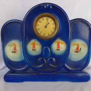 May include: A blue ceramic clock with a white face and black hands. The clock is decorated with three painted images of sailboats with red sails.