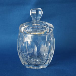 May include: A clear glass jar with a lid, featuring an etched floral design. The jar is perfect for storing sugar, honey, or other small items.