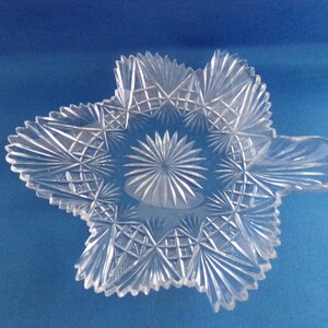 May include: A clear glass dish with a starburst design and a handle. The dish is made of cut glass and has a delicate, intricate pattern.