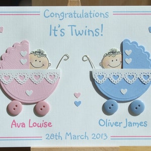 May include: A handmade card with a pink and blue baby carriage design, featuring the text "Congratulations It's Twins!" and the names "Ava Louise" and "Oliver James" with the date "28th March 2013".