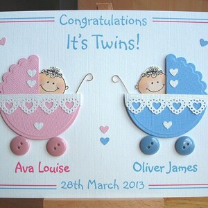 May include: A handmade card with a pink and blue baby carriage design, celebrating the birth of twins. The card features the text "Congratulations It's Twins!" and the names "Ava Louise" and "Oliver James" with the date "28th March 2013".