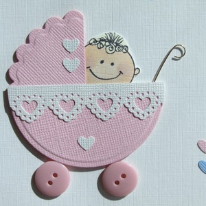May include: A pink baby carriage with a white lace trim and a smiling baby face inside. The carriage has two pink buttons for wheels and two white hearts on the side.