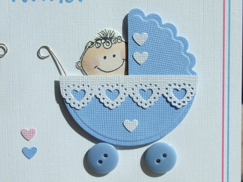 May include: A blue and white baby carriage with a white lace trim and a smiling baby face inside. The carriage has two blue buttons on the wheels.
