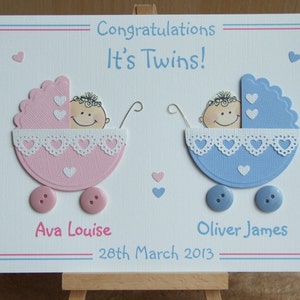 May include: A white card with a pink and blue baby carriage design. The card says "Congratulations It's Twins!" and includes the names "Ava Louise" and "Oliver James" with the date "28th March 2013".
