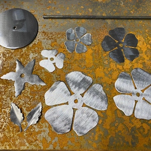 May include: A set of metal flower and leaf shapes, including a star, a circle, and several flower shapes. The shapes are all made of brushed metal and have a silver colour.