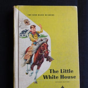 Op de afbeelding: Vintage kinderboek "The Little White House" met een gele omslag. De illustratie toont een jongen op een bruin paard, een wit huis en de tekst "The Ginn Basic Readers" en "Revised Edition".