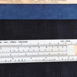 May include: Image of a wooden ruler and a chart with measurement conversions. The ruler is white with black markings and text. The chart lists conversions for long, square, surveyors, and circular measures.