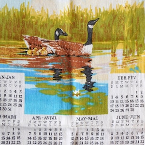 May include: A vintage calendar towel featuring a painted scene of geese swimming in a pond. The calendar displays months from January to June, with dates printed in black. The artwork includes green, blue, brown, and white colors.
