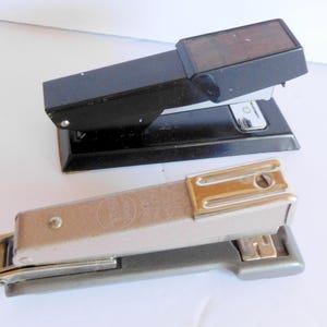May include: Two staplers, one black with a wood-look top and one silver with a chrome top.
