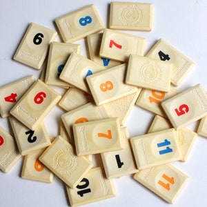 May include: A set of cream-colored tiles with black, blue, red, and orange numbers for the game Rummikub.