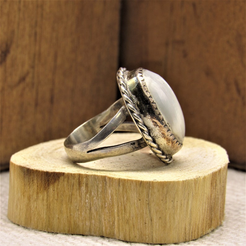 Puede incluir: Un anillo de plata con una piedra ovalada blanca engastada en un engaste de plata. El anillo tiene un dise&ntilde;o de cuerda alrededor del engaste.