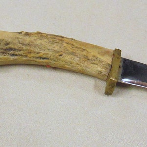 May include: A hunting knife with a curved blade and a brown antler handle. The handle has a brass guard and a brass pommel.
