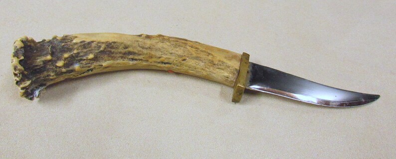 May include: A hunting knife with a curved blade and a brown antler handle. The handle has a brass guard and a brass pommel.