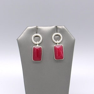May include: A pair of drop earrings featuring polished rectangular red stones set in silver-toned metal. Each earring consists of a circular silver ring at the top connected to a vertical rectangular red stone pendant with a smooth, glossy finish.