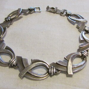 May include: A silver necklace with a geometric design. The necklace is made of interlocking loops and has a clasp closure.