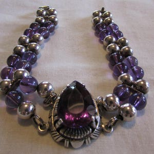 May include: A silver and purple beaded bracelet with a large, teardrop-shaped purple gemstone pendant.