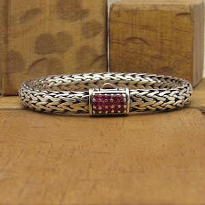 May include: A silver bracelet with a woven chain design and a clasp set with pink gemstones.