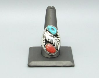 May include: A silver ring featuring a central silver feather motif flanked by a bright blue turquoise stone at the top and a vibrant red coral stone at the bottom, with small silver bead accents along the side of the feather design.