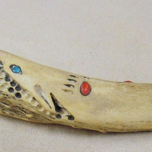 May include: A knife with a bone handle decorated with red and turquoise accents. The handle is carved with a pattern and has a bear paw print design.
