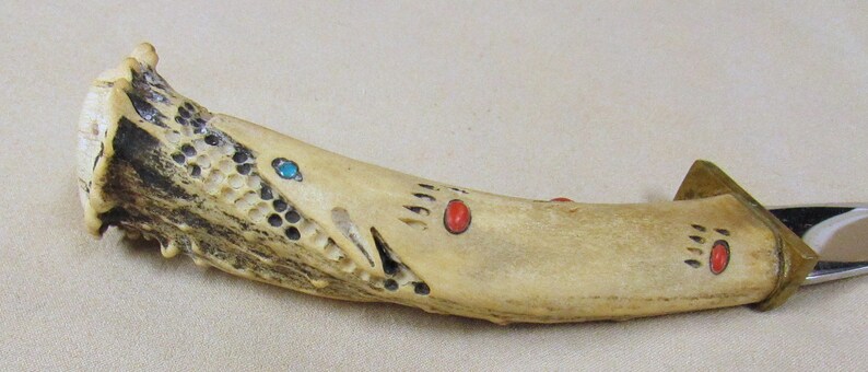 May include: A knife with a bone handle decorated with red and turquoise accents. The handle is carved with a pattern and has a bear paw print design.