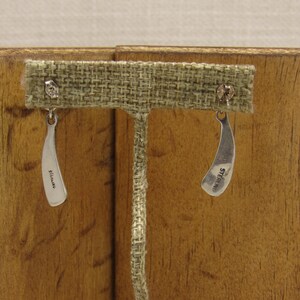 May include: A pair of silver earrings with a curved shape. The earrings are marked "STERLING" on the back.