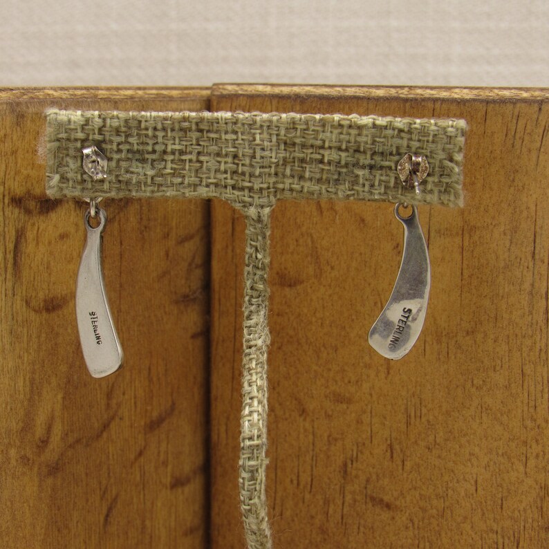 May include: A pair of silver earrings with a curved shape. The earrings are marked "STERLING" on the back.