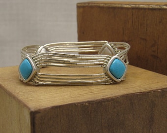 May include: A silver bracelet with turquoise stones. The bracelet is made of multiple strands of small silver beads and has two turquoise stones set in silver.