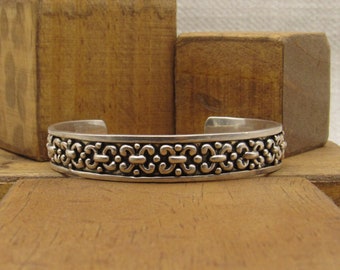 May include: A silver bracelet with a detailed, intricate design. The bracelet is made of a smooth, polished metal and has a simple, elegant style.