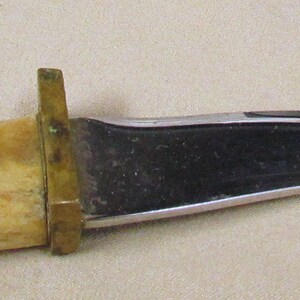 May include: A curved, black-handled knife with a bone handle. The handle is decorated with a red and black bear paw print.
