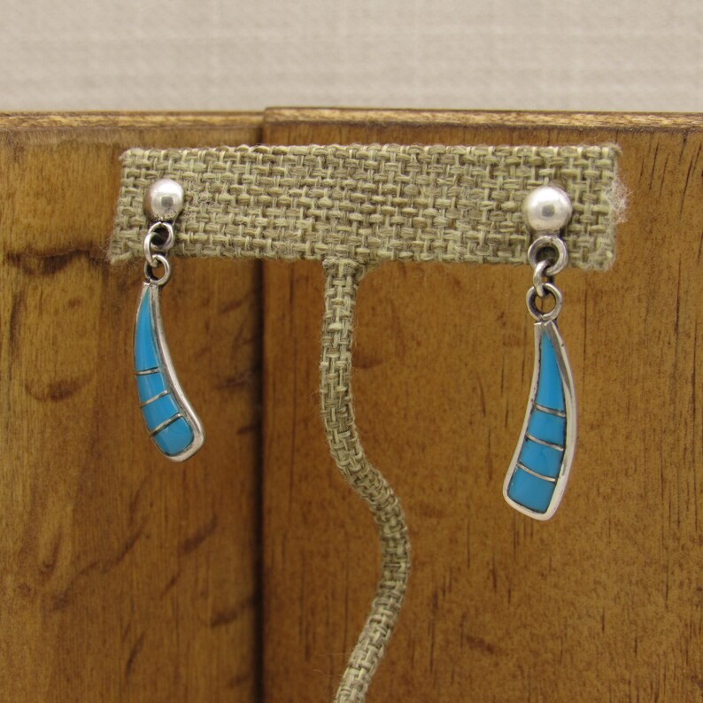 May include: A pair of silver dangle earrings with turquoise stones. The earrings are in the shape of a teardrop and have a silver bead at the top.