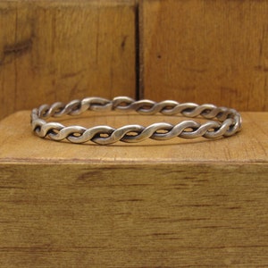 May include: A silver braided bangle bracelet. The bracelet is made of a thick, twisted silver wire.