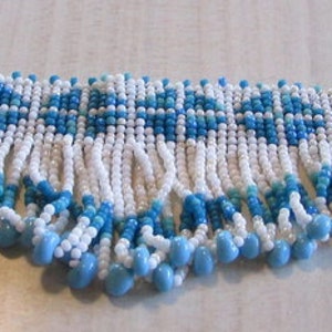 May include: A white and blue beaded necklace with a fringe of beads. The necklace is made of small, round beads and has a geometric pattern.