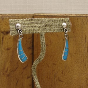 May include: A pair of silver dangle earrings with turquoise stones. The earrings are in the shape of a teardrop and have a silver bead at the top.