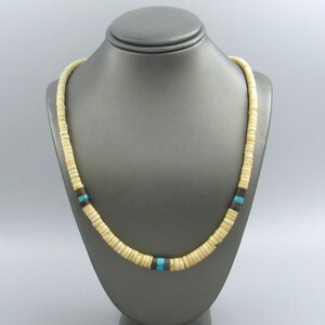May include: Cream-colored beaded necklace with turquoise and brown accents. The necklace is displayed on a gray mannequin. The beads are small and circular, with a section of turquoise and brown beads near the center.