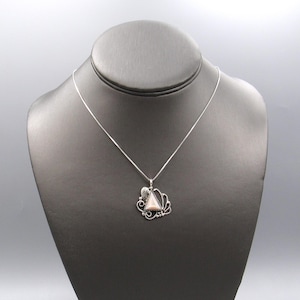 May include: A silver-toned necklace featuring a triangular pendant with a pale pink stone center. The pendant is framed by intricate metal scrollwork and a small leaf detail at the top, suspended from a thin, delicate silver-toned chain.