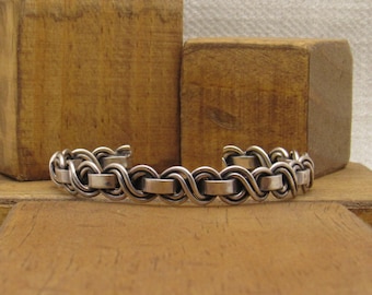 May include: A silver bracelet with a braided design. The bracelet is made of multiple strands of silver wire that are woven together to create a rope-like effect.