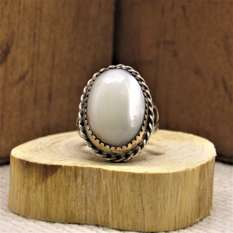 Puede incluir: Un anillo de plata con una piedra ovalada blanca engastada en un dise&ntilde;o de cuerda.