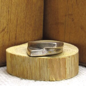 May include: A silver ring with a unique, angular design. The ring is sitting on a wooden surface.